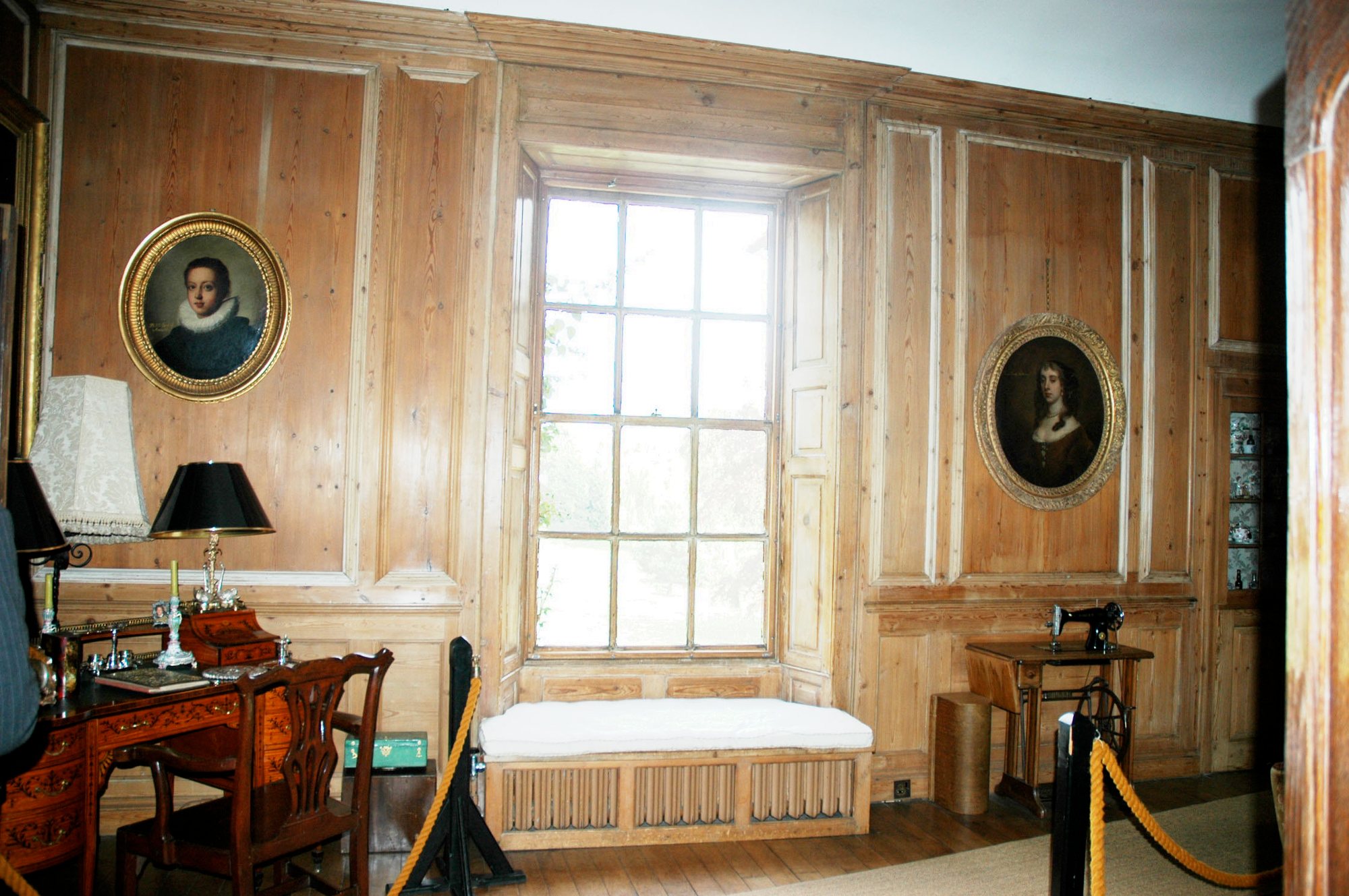 A light panelled room with portraits and a window seat